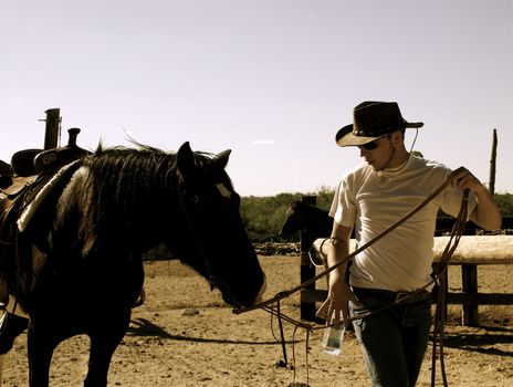 Cowboy wearing white T shirt, Levis and stetson leading horse by the reins