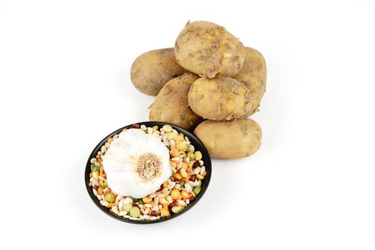 Small pile of brown unpeeled potatoes with soup pulses and garlic on a reflective white background