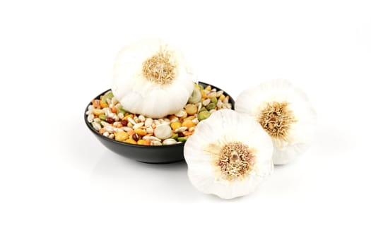 White raw garlic bulbs with a small black dish of soup pulses on a reflective white background