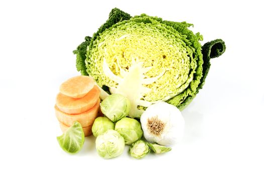 Half a raw green cabbage with garlic bulb, sprouts and slices of sweet potato on a reflective white background