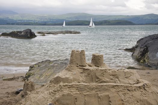 Sandcastle on the beach,with sea, yachts and mountains in the background.