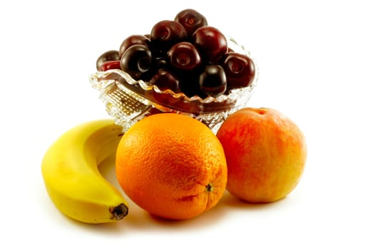 The banana, orange, peach and vase with a sweet cherry are photographed on a white background