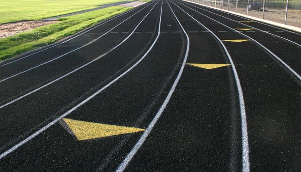 Black high school track showing lane markings with shadows of previous markings visible with arrows coming toward viewer.