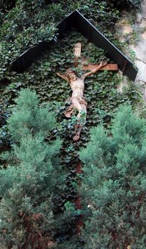 Cross with a statue of saint on the wall with a wild wine