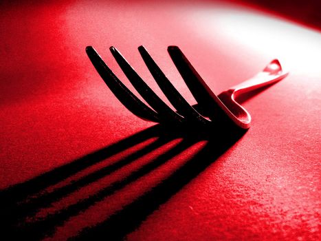 Dinner fork in direct light with long shadow against a red textured background