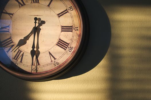 Antique Clock on an olive green wall with dramatic evening light and shadows.