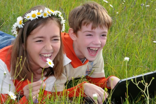 pigeon pair with a wreath from camomiles lie with a computer on a grass and laugh loudly