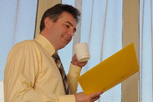 man in a tie on a background a window with a white cup and yellow folder