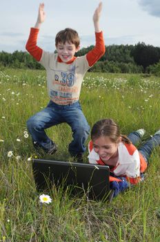 a pigeon pair lie on a green grass among the colors of the field and peep in the screen of notebook