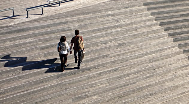 two peoples with long shadows walking on the wooden stairs