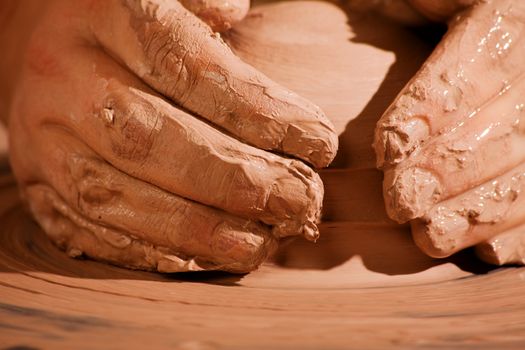 Hands forming wet clay on pottery wheel