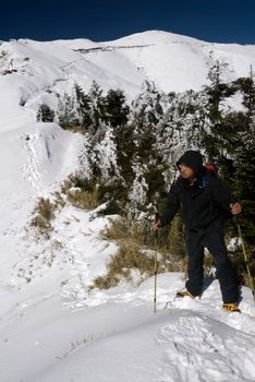 Man stand on snow mountain top and walk with backpack and trekking pole.