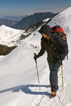 Mountaineer walk on snow path on mountain with trekking pole.