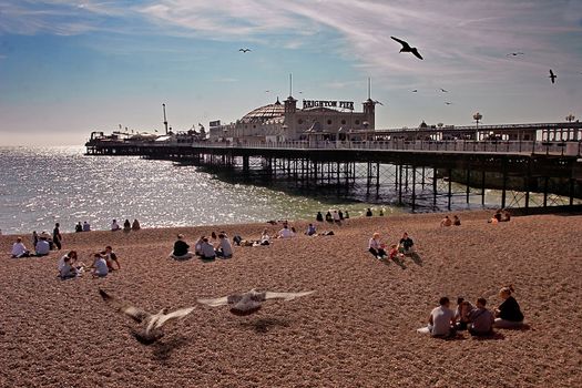 Families relax at the seaside beside Brighton Pier in Sussex England.