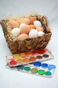 A wicker basket with fresh eggs and different colors of paint