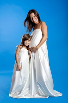 Beautiful pregnant woman with her little daughter isolated on a blue background
