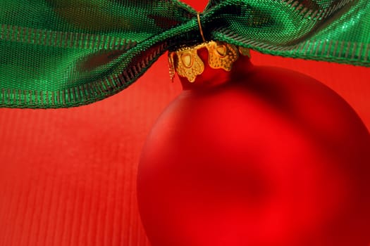 Close up of a red ornament with green ribbon on a red background.
