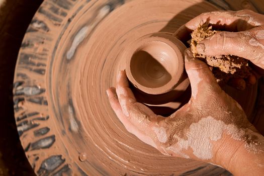 Hands forming clay pot on pottery wheel