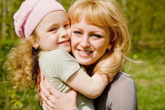 The beautiful little girl in a pink cap embraces mum with light hair
