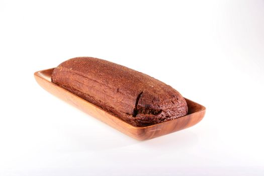 Loaf of black bread of the oblong form in a wooden plate on a white background.