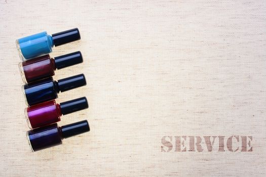 Small bottles with a multi-coloured varnish for manicure against from a fabric with an inscription service.