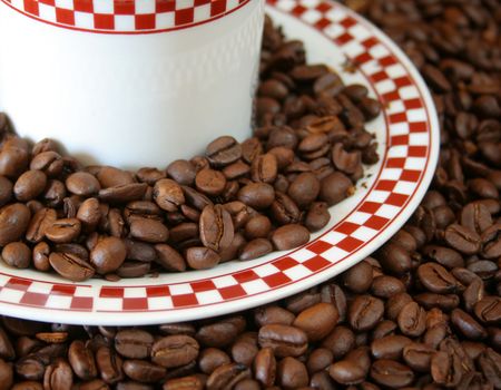 plate full of coffee beans with a coffee cup in the middle along with a background coffee beans.


