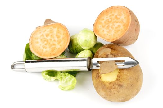 Small brown raw potato with chrome peeler and a sweet potato cut in half with sprouts on a reflective white background