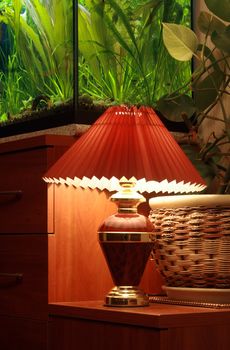 Evening home interior with luminous table lamp and aquarium