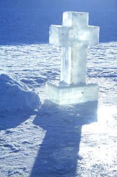 Cross made from ice standing on snow background