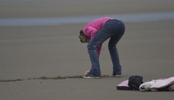 Young girl writing in the sand, her belongings thrown behind her.