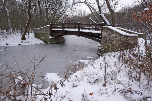 Beautiful Wooden Bridge Over Frozen Stream on Blustry Winter Day
