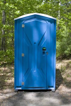 A blue porta potty located on the wooded hiking trail.