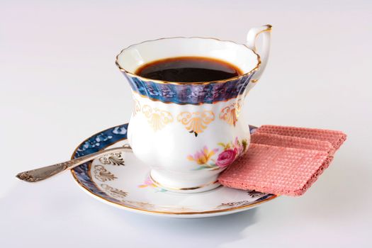 Ceramic cup with black coffee and a spoon on a saucer, a wafer as a dessert.