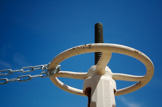 Industrial Valve & Chain Abainst A Deep Blue Sky.