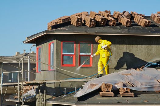 Construction worker pressure washes fresh applied surface of new home exterior.