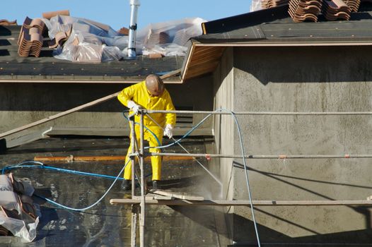 Construction worker pressure washes fresh applied surface of new home exterior.