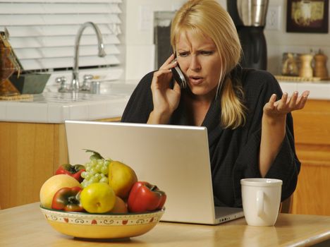 Woman in her kitchen on cell phone sitting in front of laptop. Computer problems?