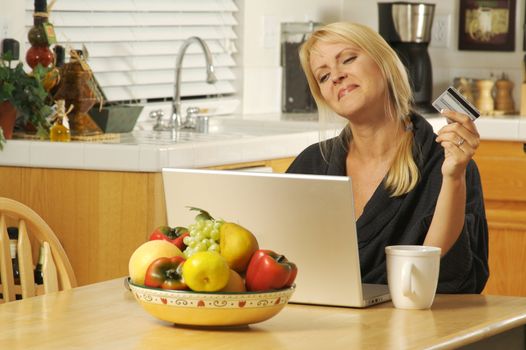 Woman holding credit card in her kitchen Using her Laptop for Ecommerce.