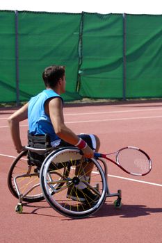 A wheelchair tennis player during a tennis championship match, waiting to take a shot.