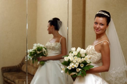 The beautiful bride with a wedding bouquet from white tulips with reflection in a mirror