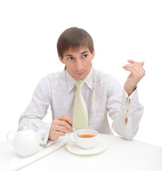 Young handsome  confident  man on white background. He sits for white table and drink tea from white cup.