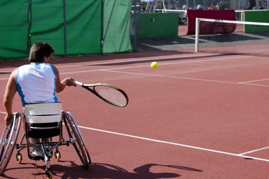 A wheelchair tennis player during a tennis championship match, taking a shot.