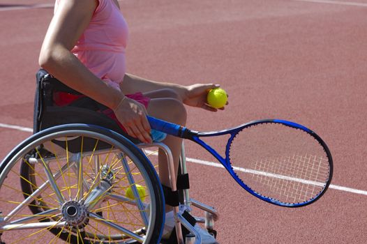Detail of a wheelchair tennis player about to serve during a tennis championship match. Space for text on the plain area of the court behind her.