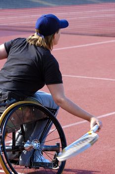 A wheelchair tennis player during a tennis championship match, returning a shot. Motion blur on her racket.