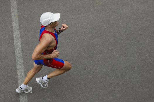 A marathon runner crossing a line, taken from above. Motion blur on his feet. Space for text on the tarmac in front of him.
