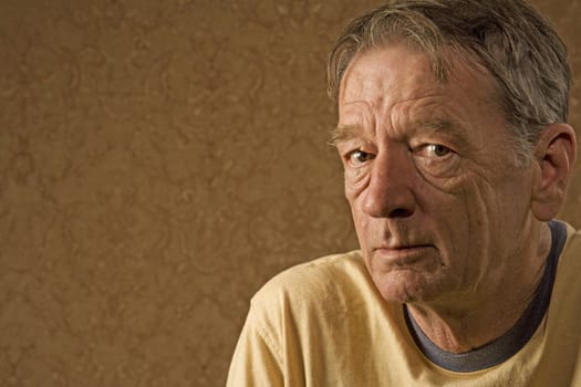 Man with a craggy face wearing a yellow shirt against a gold background with copy space