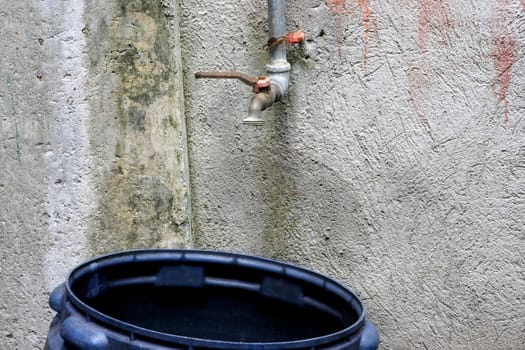 Rusty old Faucet with Plastic Bucket outside the house