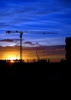 Cranes and construction site silhouette against setting (or rising) sun