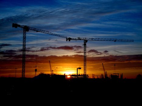 Cranes and construction site silhouette against setting (or rising) sun