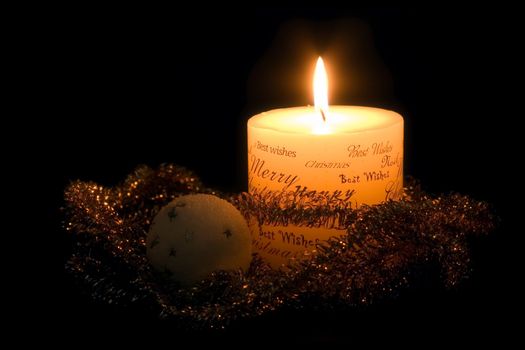 Lit white Christmas candle, golden ribbon and white christmas ball, on black background